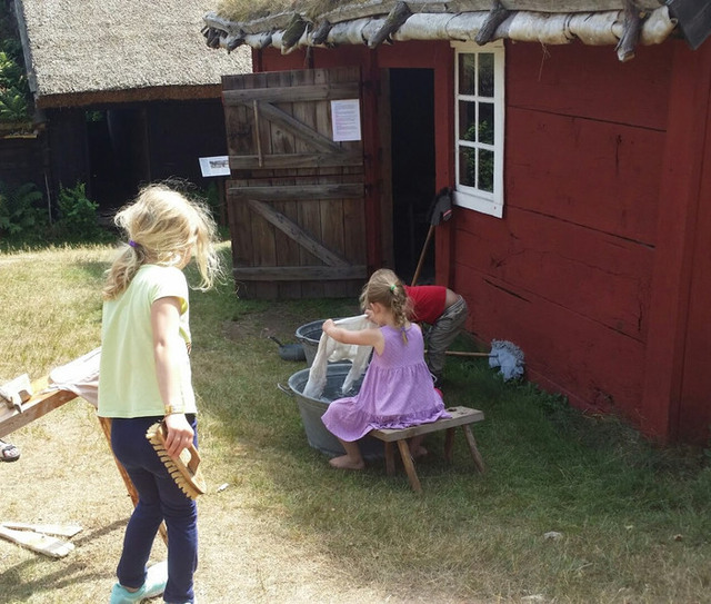 Två barn med långt hår fotograferade bakifrån när de interagerar med den kulturhistoriska miljön på Hallandsgården i Halmstad.