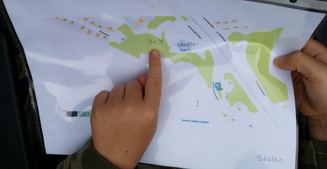 En barnhand pekar på ett kartblad som ligger i en plastficka.