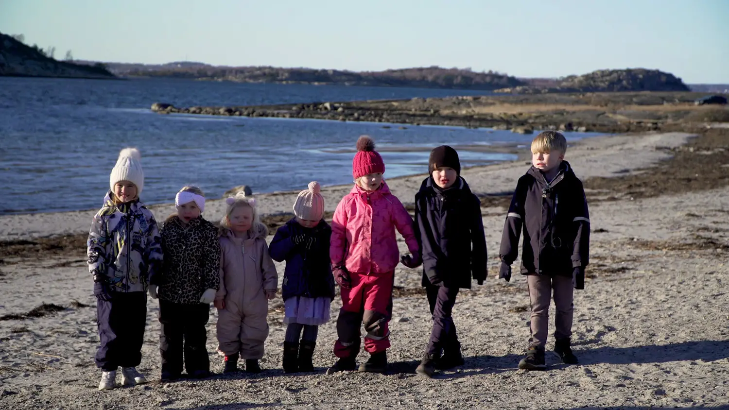 Sju förskolebarn i mössor och vinterkläder på en strand i Åsa, Halland.