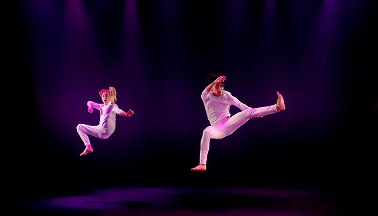 Två dansare i vita kläder hoppar upp i luften.