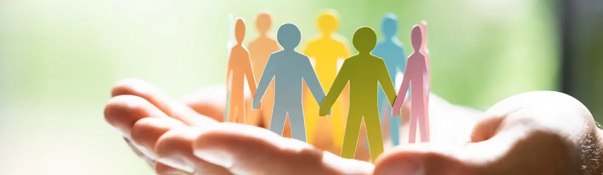 En hand håller en cirkel med olikfärgade pappfigurer som håller varandra i handen.