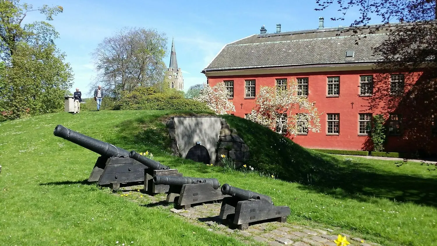 Slottsträdgården vid Halmstads slott med fyra kanoner i förgrunden, två personer skymtar långt bak i bilden.