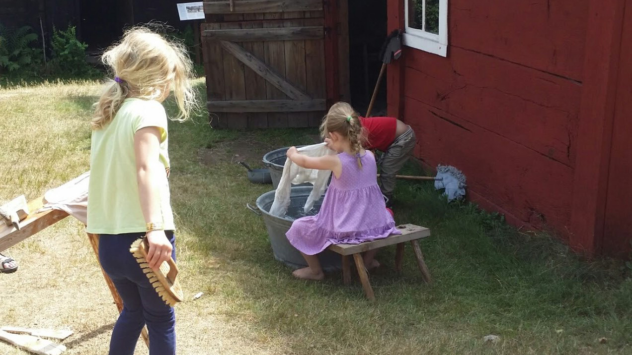 Två barn med långt hår fotograferade bakifrån när de interagerar med den kulturhistoriska miljön på Hallandsgården i Halmstad.