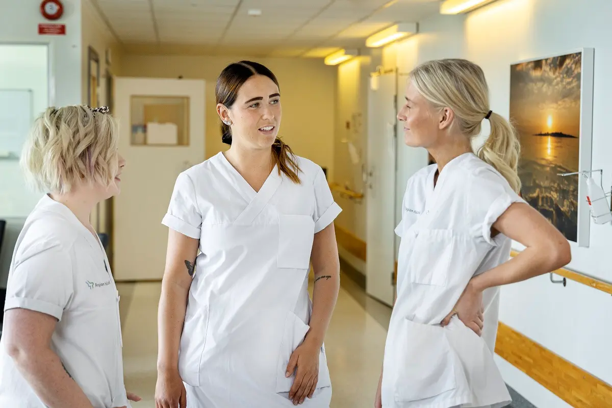 Tre sjuksköterskor i korridor, pratar med varandra