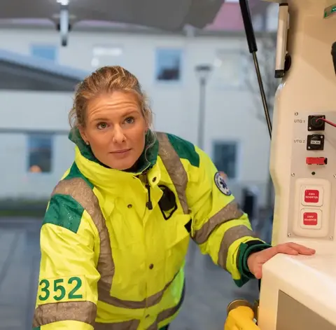 Kvinnlig ambulanssköterska i gul jacka ser in i en ambulans