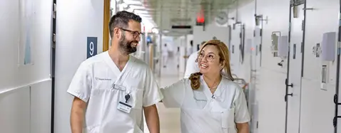 En man och en kvinna i vita vårdkläder går framåt i en sjukhuskorridor