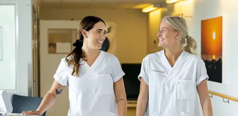 Två kvinnor i vita vårdkläder i en sjukhuskorridor.