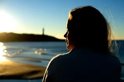 Ung flicka i solnedgången, hav och en fyr i bakgrunden.